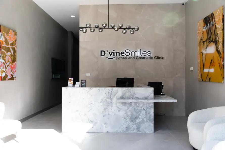 Elegant reception area of D'vine Smiles Clinic featuring a modern stone desk, flower arrangement, and clinic signage.