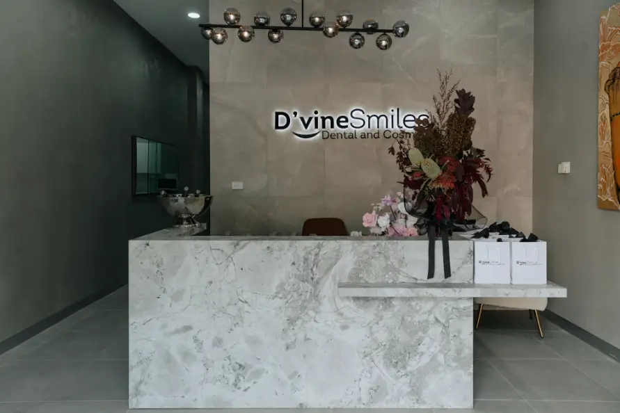 Elegant reception area of D'vine Smiles Clinic featuring a modern stone desk, flower arrangement, and clinic signage.